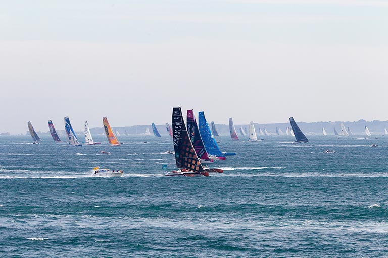 "Départ de la Route du Rhum avec une flotte de voiliers multicoques et monocoques naviguant au large de Saint-Malo